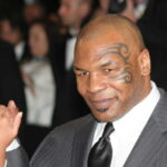 A man in a suit with a distinctive tattoo on his face, holding hands with a child