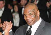 A man in a suit with a distinctive tattoo on his face, holding hands with a child