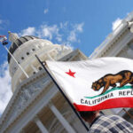 California state flag held up in front of a government building under a blue sky