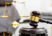 A wooden gavel resting on a sound block with a blurred scale of justice in the background