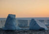 Two icebergs floating in the ocean at sunset