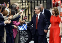 Couple holding hands greeting people waving flags