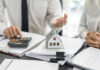 Mini house model on documents with two people discussing finances