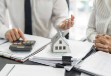 Mini house model on documents with two people discussing finances