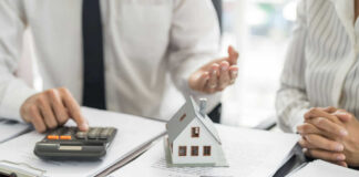 Mini house model on documents with two people discussing finances