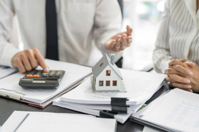 Mini house model on documents with two people discussing finances