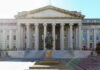 A historical statue in front of a large government building with columns