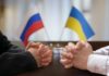 Two pairs of hands clasped together with Russian and Ukrainian flags in the background