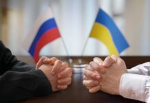 Two pairs of hands clasped together with Russian and Ukrainian flags in the background