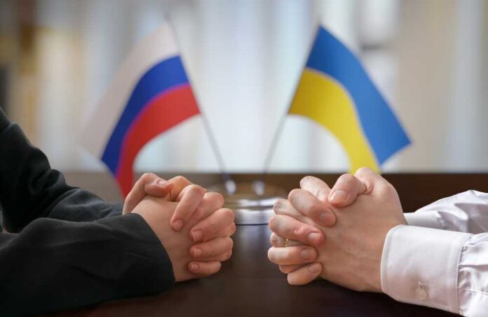 Two pairs of hands clasped together with Russian and Ukrainian flags in the background