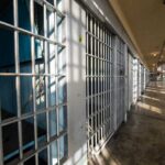 Interior view of a prison corridor with jail cells and sunlight streaming through windows
