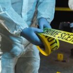 Forensic investigator in protective gear handling crime scene tape