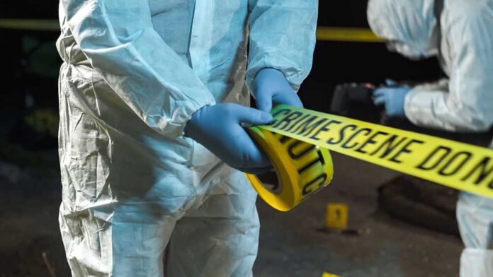 Forensic investigator in protective gear handling crime scene tape