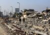 Two individuals walking through a devastated urban area filled with rubble