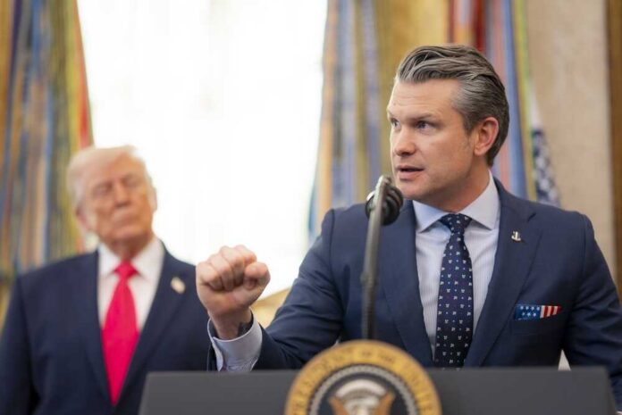 A man in a suit delivering a speech at a podium with a presidential seal, while another man stands in the background.