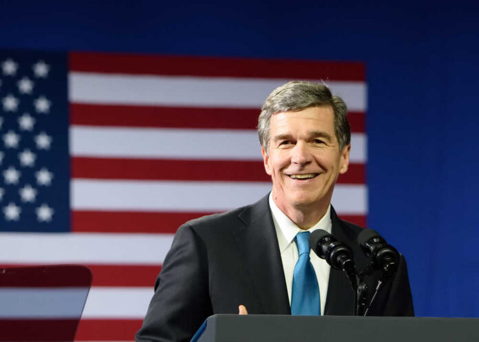 A smiling politician speaking at a podium with an American flag in the background