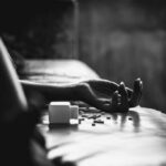 Hand on bed beside spilled pill bottle and tablets