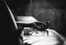 Hand on bed beside spilled pill bottle and tablets