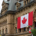 Historic building with large Canadian flags displayed outside