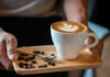 Latte with latte art on a wooden tray with coffee beans and a spoon