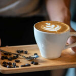 Latte with latte art on a wooden tray with coffee beans and a spoon