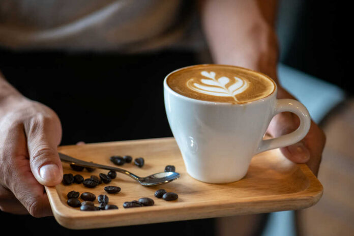 Latte with latte art on a wooden tray with coffee beans and a spoon