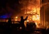 Firefighters battle a massive blaze amid burning cars and collapsed structure at night
