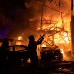 Firefighters battle a massive blaze amid burning cars and collapsed structure at night