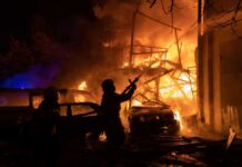 Firefighters battle a massive blaze amid burning cars and collapsed structure at night