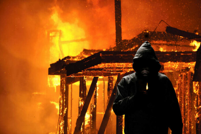 Hooded figure holding lighter in front of fire