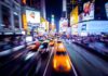 Yellow taxis speed through a neon-lit city street at night