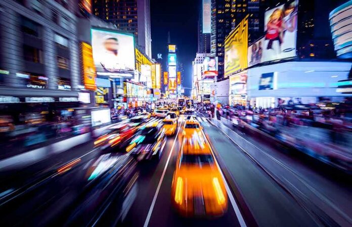 shutterstock_1036558993 Yellow taxis speed through a neon-lit city street at night
