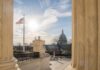 U.S. Capitol seen between marble columns with flag and statue in foreground