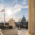 U.S. Capitol seen between marble columns with flag and statue in foreground