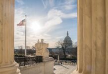 U.S. Capitol seen between marble columns with flag and statue in foreground