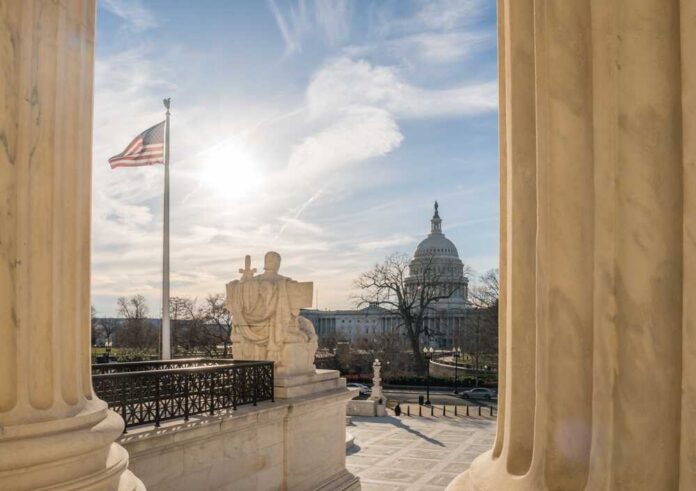 U.S. Capitol seen between marble columns with flag and statue in foreground