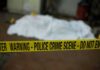 crime scene tape in foreground with covered body in background