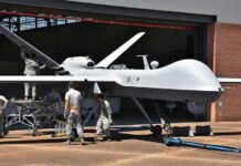 Military drone being serviced by ground crew outside a hangar