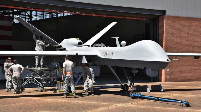Military drone being serviced by ground crew outside a hangar