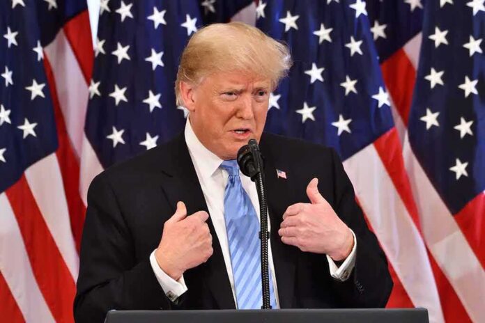 man in suit speaking at podium with US flags behind