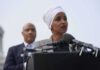 Woman in white headwrap speaking at microphones outdoors