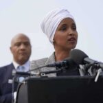 Woman in white headwrap speaking at microphones outdoors