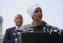 Woman in white headwrap speaking at microphones outdoors