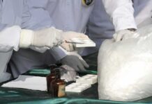 Scientists in lab coats handling white powder sample with tools