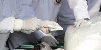 Scientists in lab coats handling white powder sample with tools