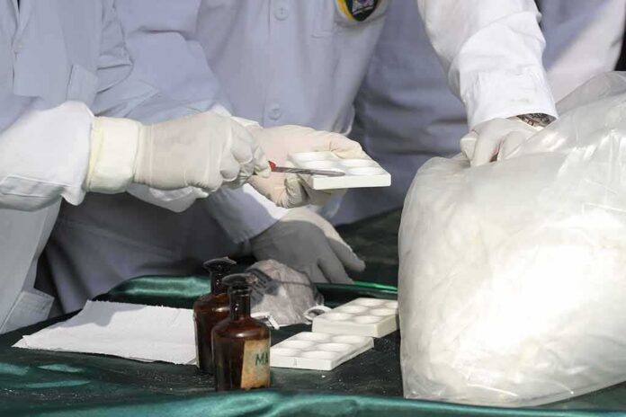 Scientists in lab coats handling white powder sample with tools