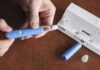 Hands assembling a blue insulin pen with packaging on a table