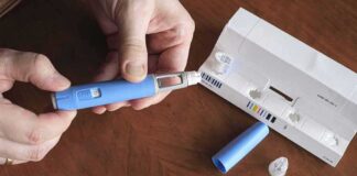 Hands assembling a blue insulin pen with packaging on a table