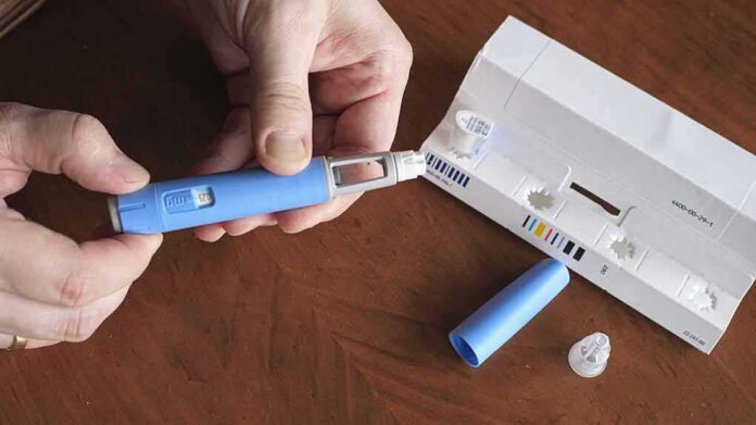 shutterstock_2151232809 Hands assembling a blue insulin pen with packaging on a table