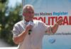 Man speaking on an outdoor stage with a microphone